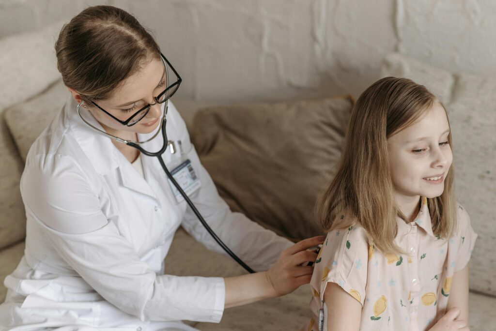 A doctor with a stethoscope examining a smiling girl during a medical check-up at home.