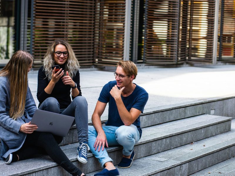 Three young professionals having a friendly chat while sitting on outdoor steps.