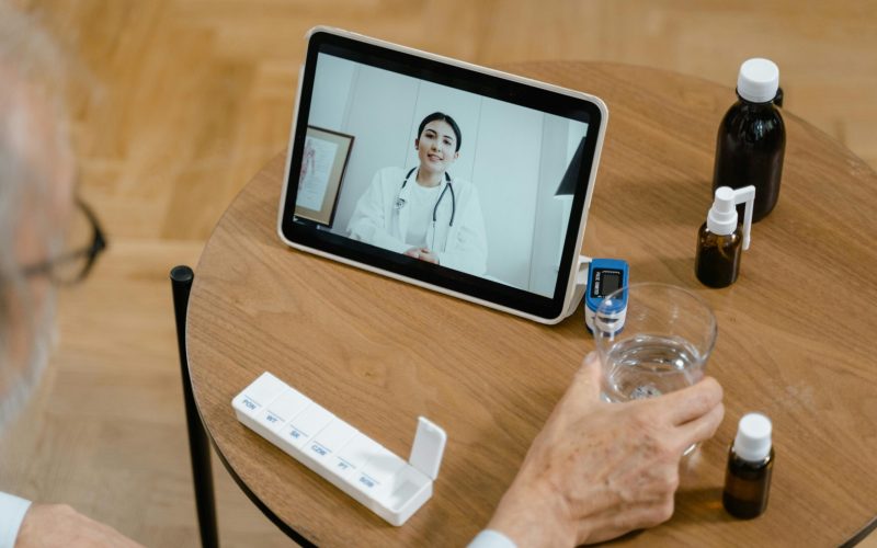 Senior adult having a virtual doctor consultation on a tablet with medications on the table.